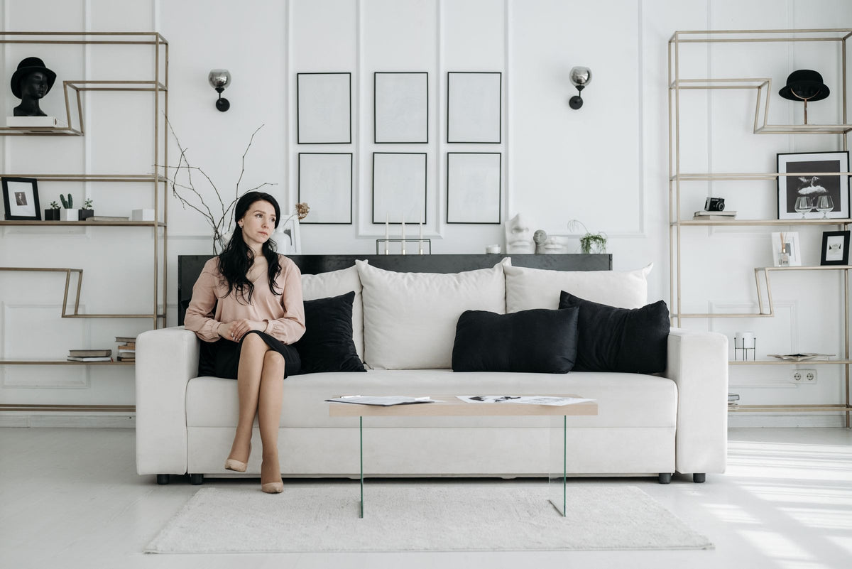 Femme dans un salon blanc, canapé et étagères dorées