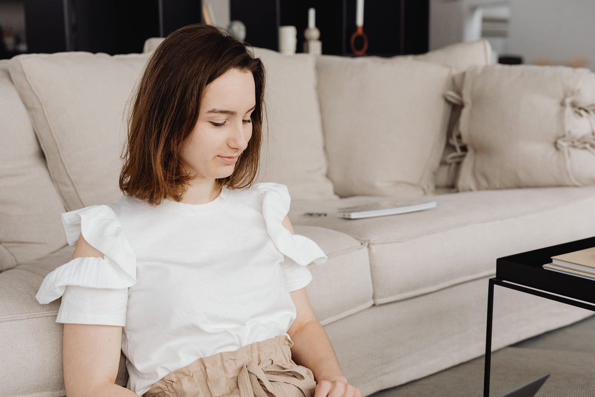Femme assise dans un canapé beige, dans un salon clair